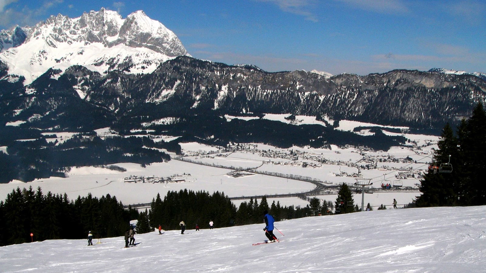 Skiløbere på en bred, præpareret piste i Tyrol med Wilder Kaiser-bjergene i baggrunden